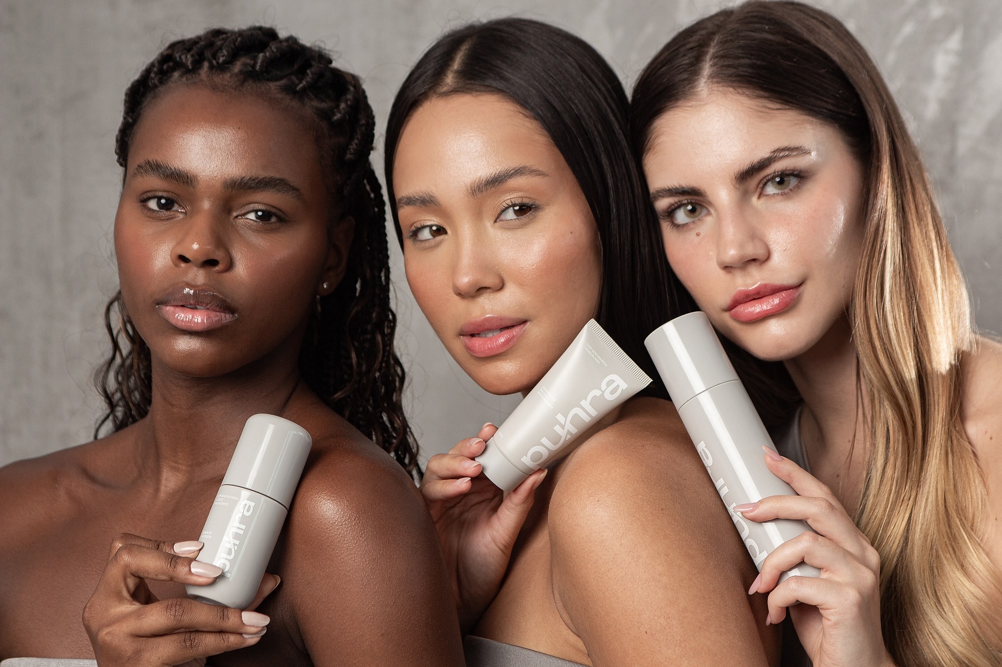 Três mulheres com peles diferentes segurando produtos da linha Puhra