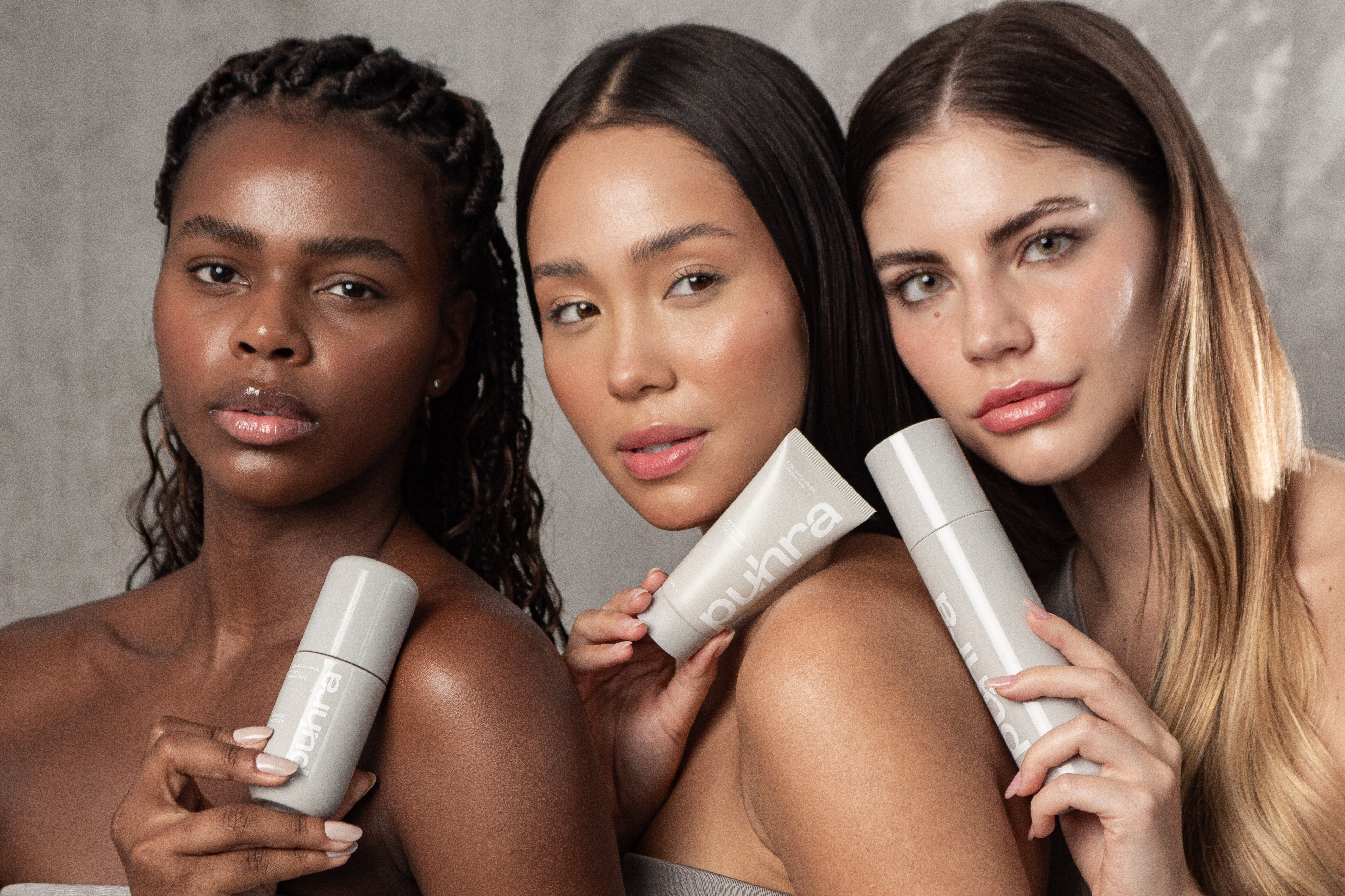 Três mulheres com peles diferentes segurando produtos da linha Puhra