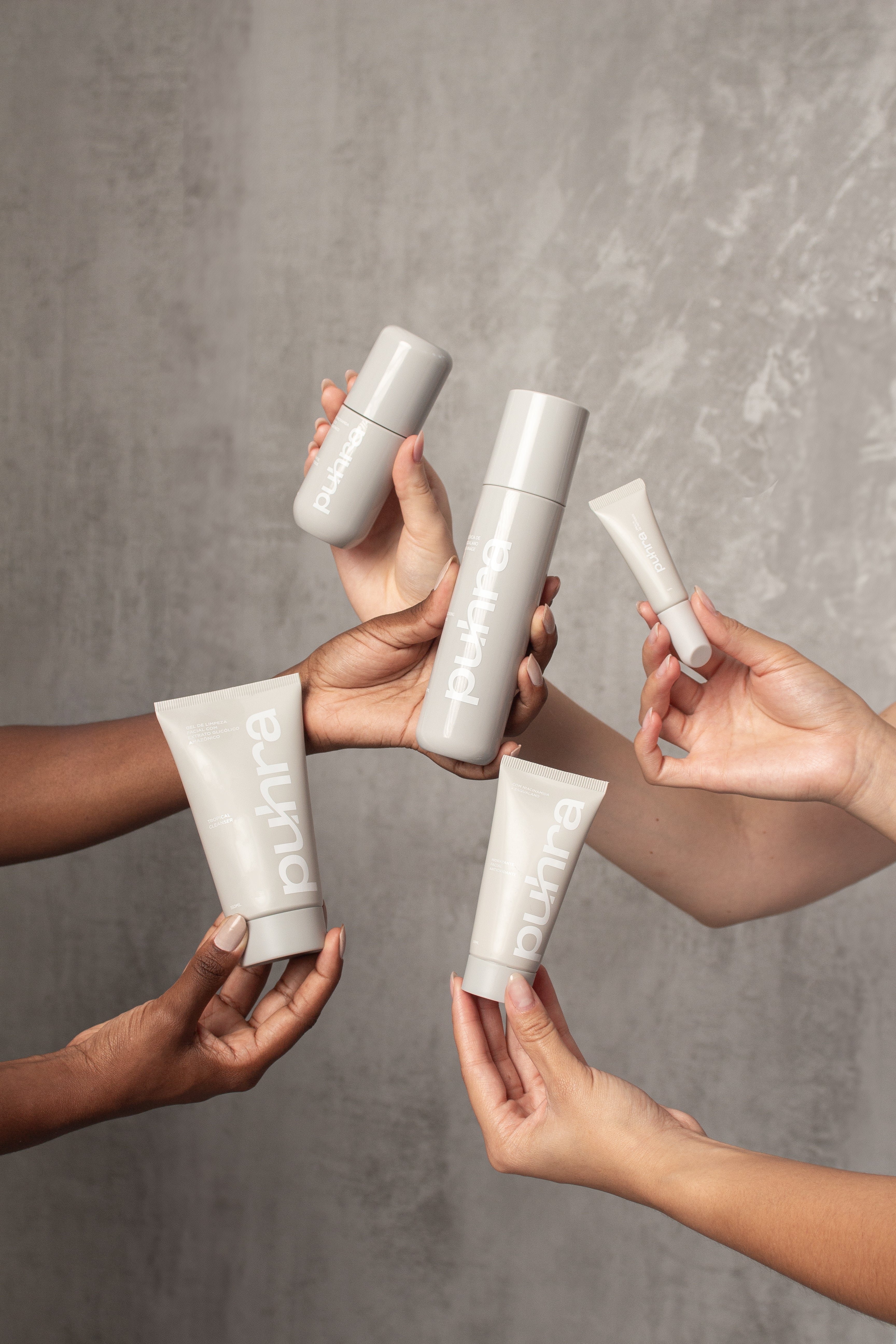 Kit de skincare Puhra com cinco produtos (dois tubos, um frasco spray, um sérum e um contorno de olhos) ao lado de necessaire cinza da marca